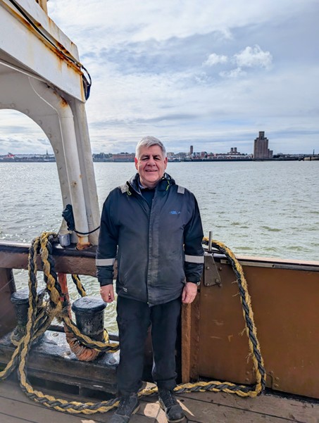 Dan Evans, Customer Service Officer on the deck of the ferry with Wirral in the background.